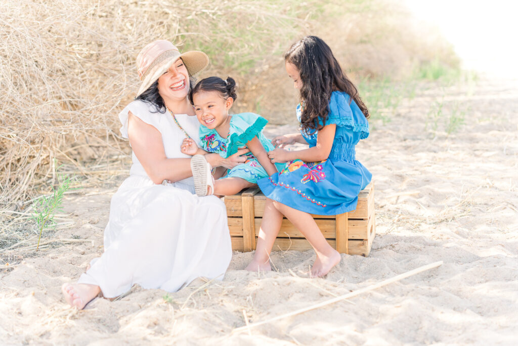 Mom prepped kids for their family session. Mom and her two daughters smiling, laughing and tickling each other during a family session in Las Cruces, New Mexico.